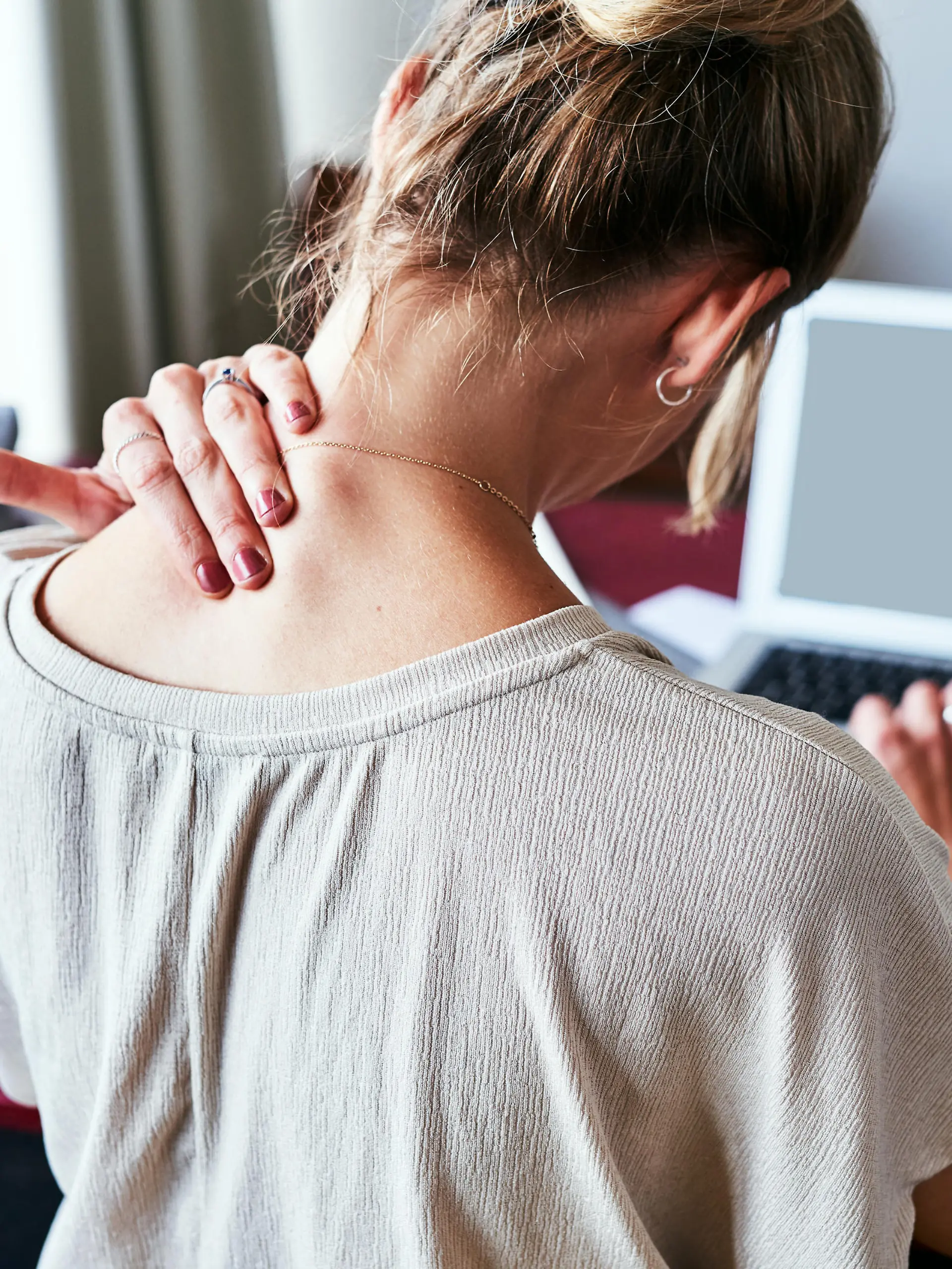 Rearview shot of a designer experiencing discomfort in her shoulders while sitting at her desk