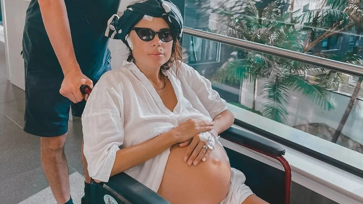 Elise wird in einem Rollstuhl geschoben während sie sich ihren Schwangerschaftsbauch hält.
