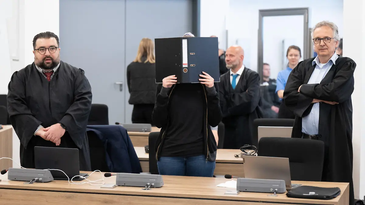 31.05.2023, Sachsen, Dresden: Die Angeklagte (M) steht bei der Fortsetzung des Prozesses im Oberlandesgericht (OLG) Dresden im Verhandlungssaal und hält einen Aktenordner vor ihr Gesicht. Die Gruppe bestehend aus Lina E. und drei Männern aus der linksextremistischen Leipziger Szene ist wegen Mitgliedschaft in einer kriminellen Vereinigung angeklagt. Foto: Sebastian Kahnert/dpa +++ dpa-Bildfunk +++