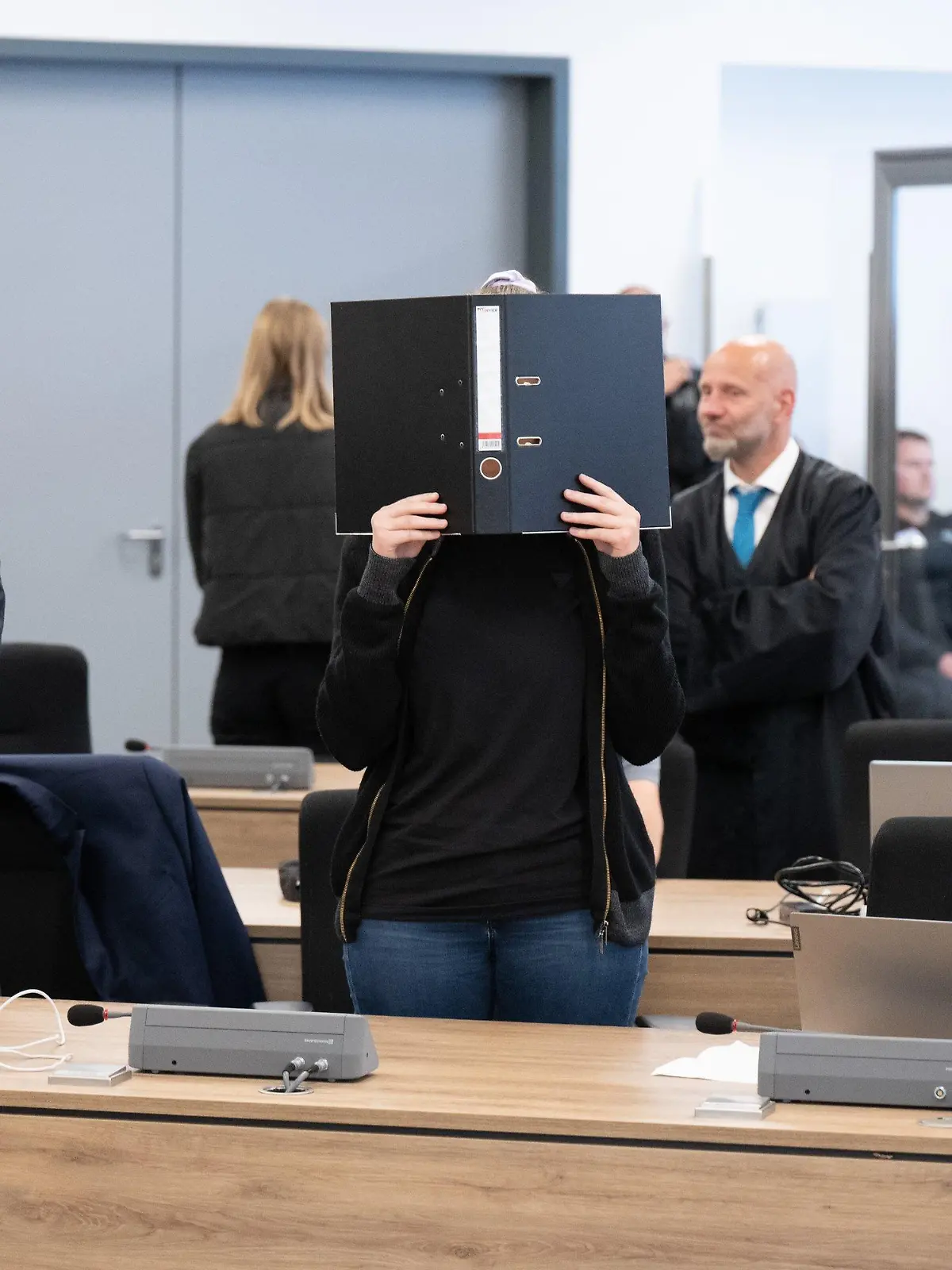 31.05.2023, Sachsen, Dresden: Die Angeklagte (M) steht bei der Fortsetzung des Prozesses im Oberlandesgericht (OLG) Dresden im Verhandlungssaal und hält einen Aktenordner vor ihr Gesicht. Die Gruppe bestehend aus Lina E. und drei Männern aus der linksextremistischen Leipziger Szene ist wegen Mitgliedschaft in einer kriminellen Vereinigung angeklagt. Foto: Sebastian Kahnert/dpa +++ dpa-Bildfunk +++