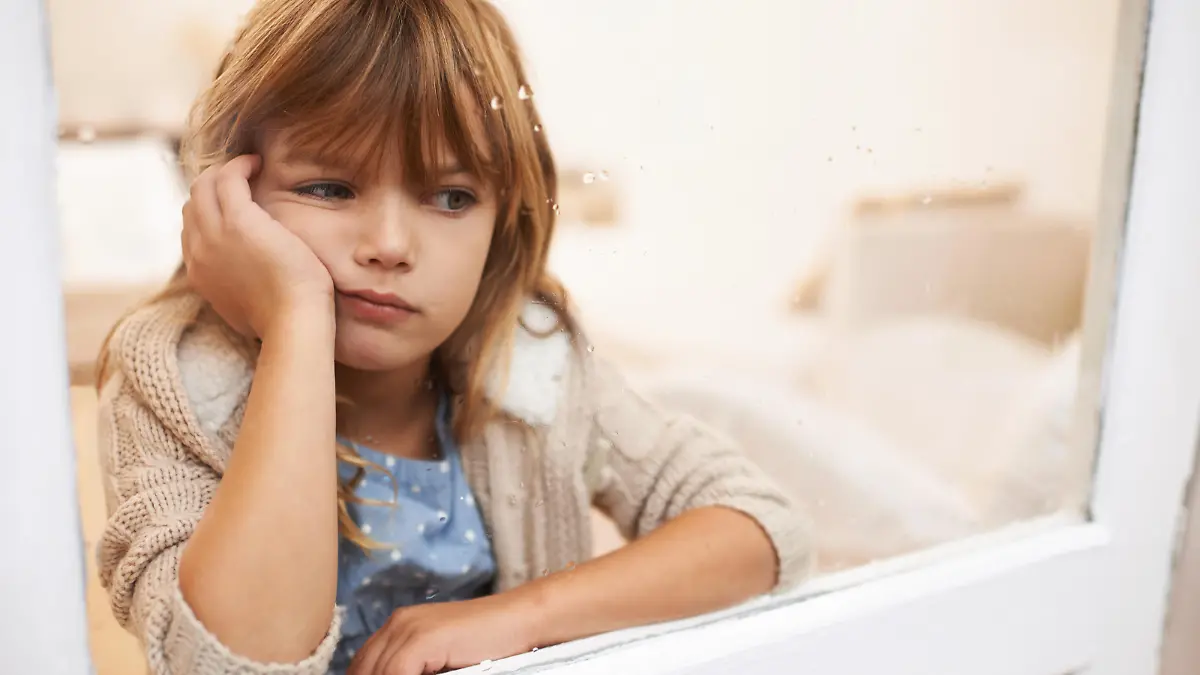 Shot of a bored-looking little girl sitting and looking out a window on a rainy day