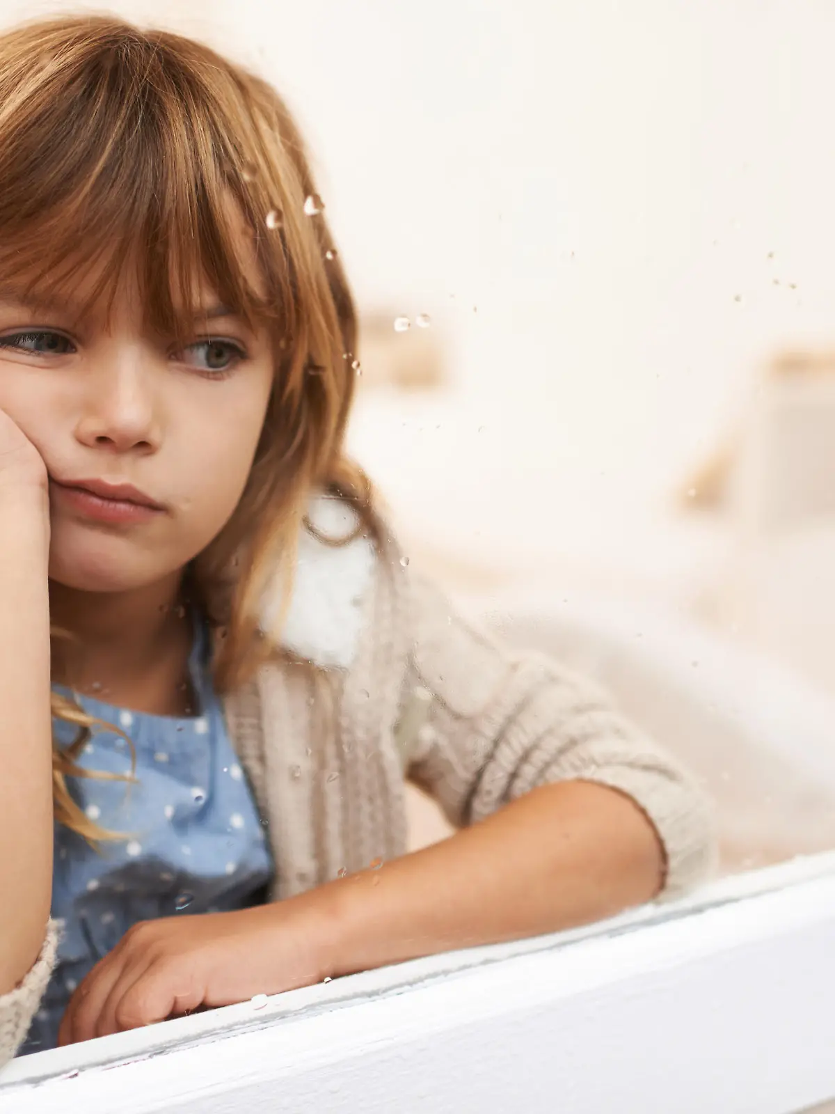 Shot of a bored-looking little girl sitting and looking out a window on a rainy day