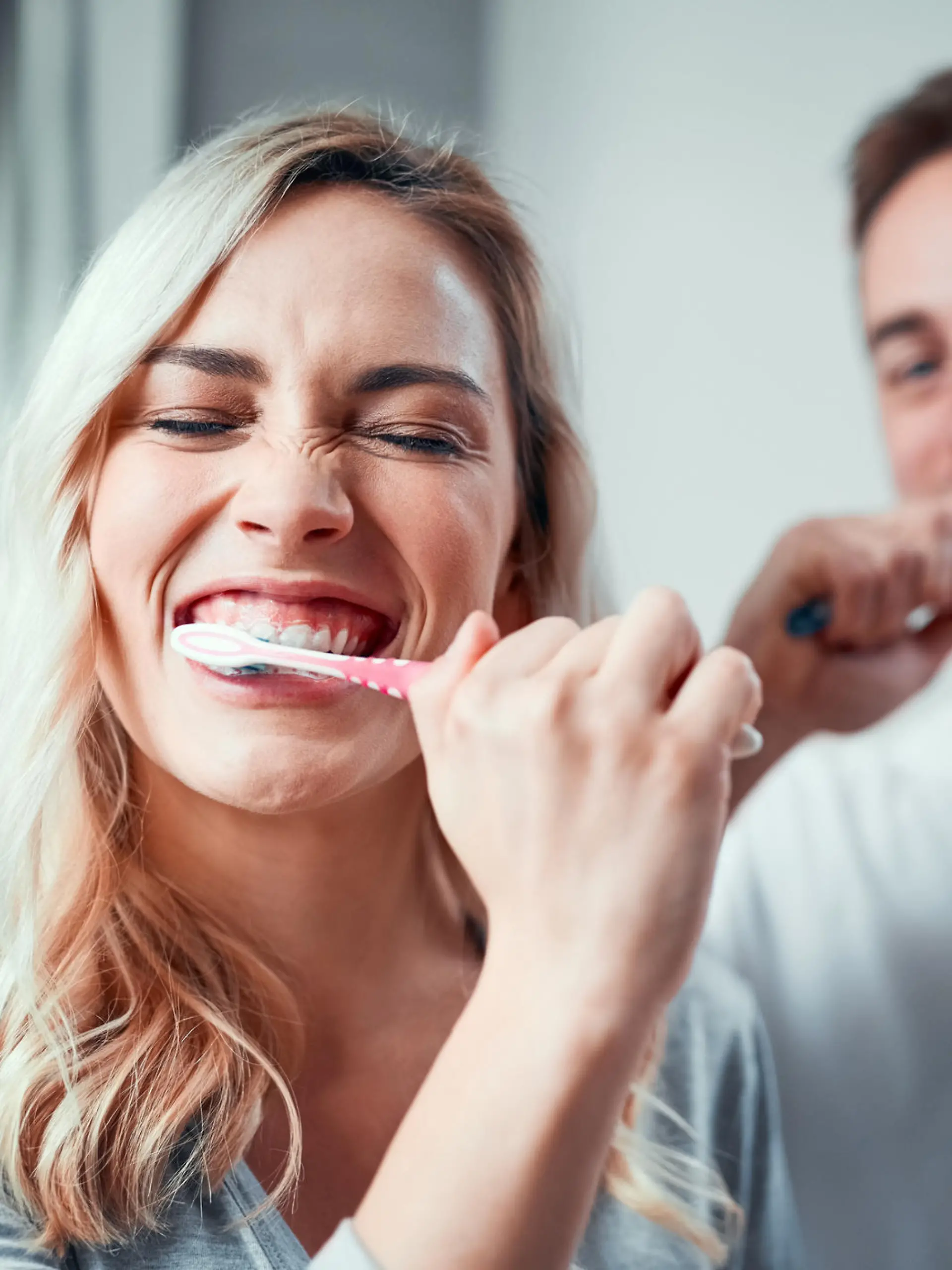 Frau und Mann stehen im Bad und putzen sich die Zähne.