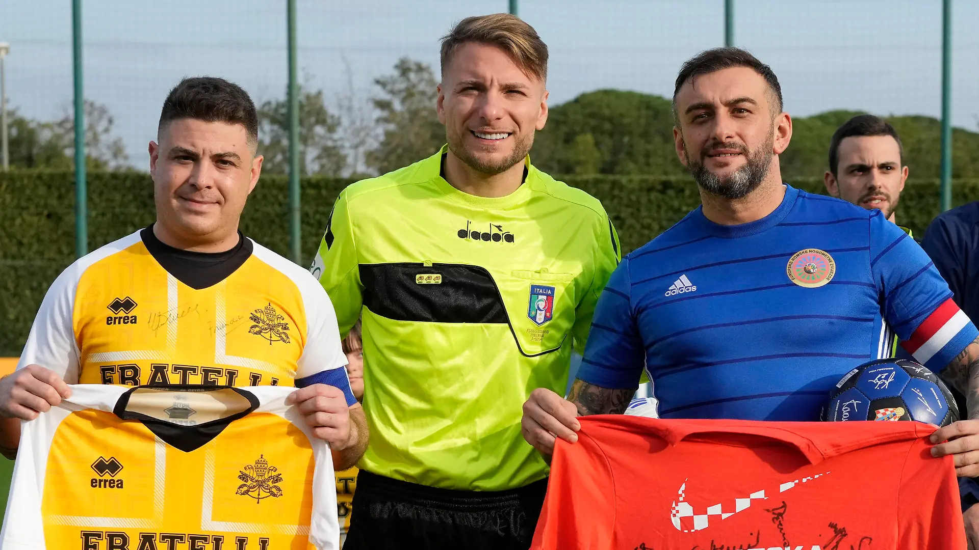 Lazio captain Ciro Immobile, center, poses for a photo with the captains of the Vatican soccer team "Fratelli Tutti" (All Brothers), left, and the World Rom Organization team prior to the start of the "Brothers All" friendly match, at the Italian top league Lazio soccer training facility, in Formello, outskirts of Rome, Sunday, Nov. 21, 2021. The "Brothers All" friendly is an extension of Pope Francis' effort to promote dialogue and fraternity, including through sport, and coincides with Lazio's effort to combat racism and discrimination in soccer. (AP Photo/Andrew Medichini)