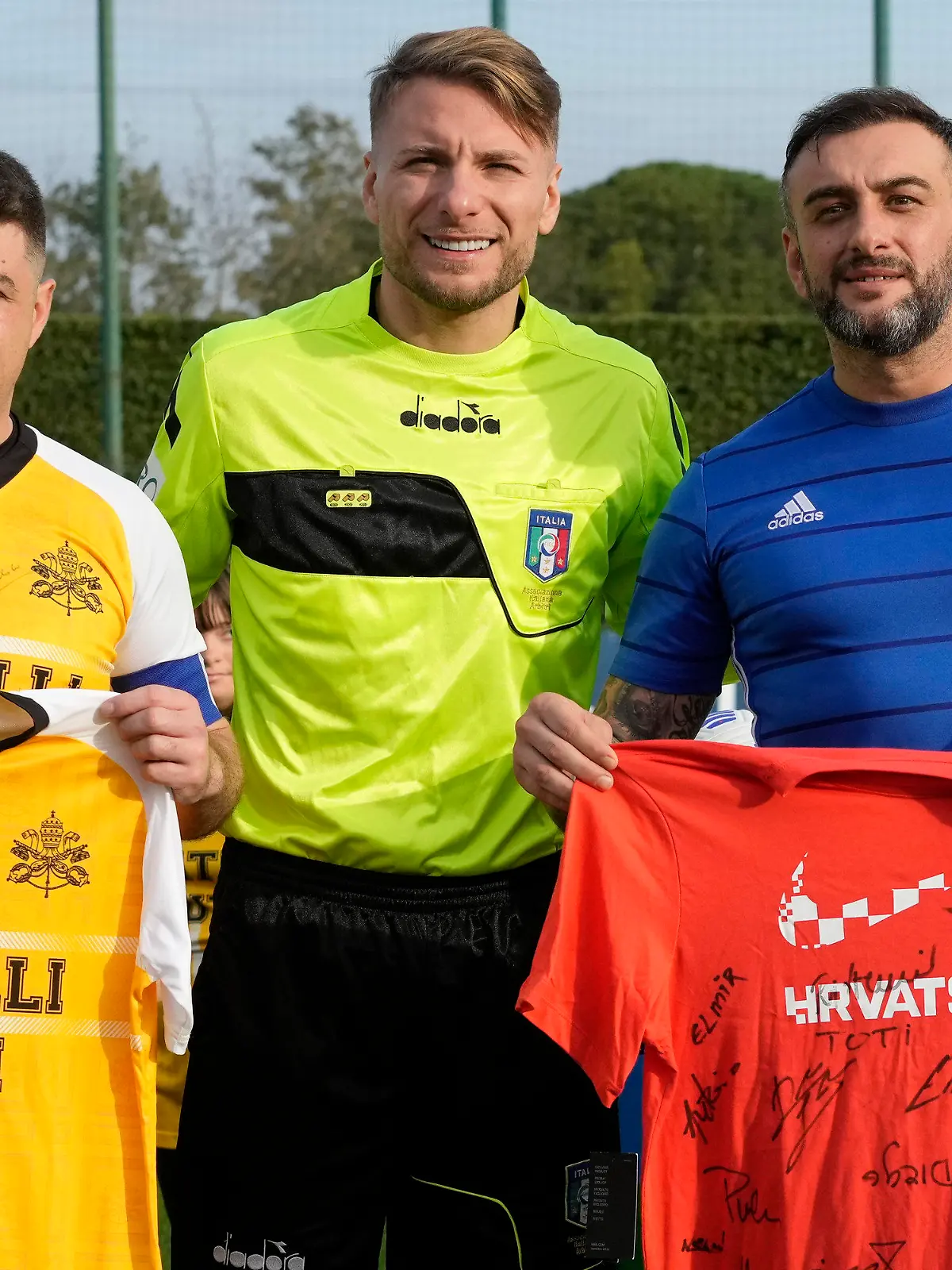 Lazio captain Ciro Immobile, center, poses for a photo with the captains of the Vatican soccer team "Fratelli Tutti" (All Brothers), left, and the World Rom Organization team prior to the start of the "Brothers All" friendly match, at the Italian top league Lazio soccer training facility, in Formello, outskirts of Rome, Sunday, Nov. 21, 2021. The "Brothers All" friendly is an extension of Pope Francis' effort to promote dialogue and fraternity, including through sport, and coincides with Lazio's effort to combat racism and discrimination in soccer. (AP Photo/Andrew Medichini)