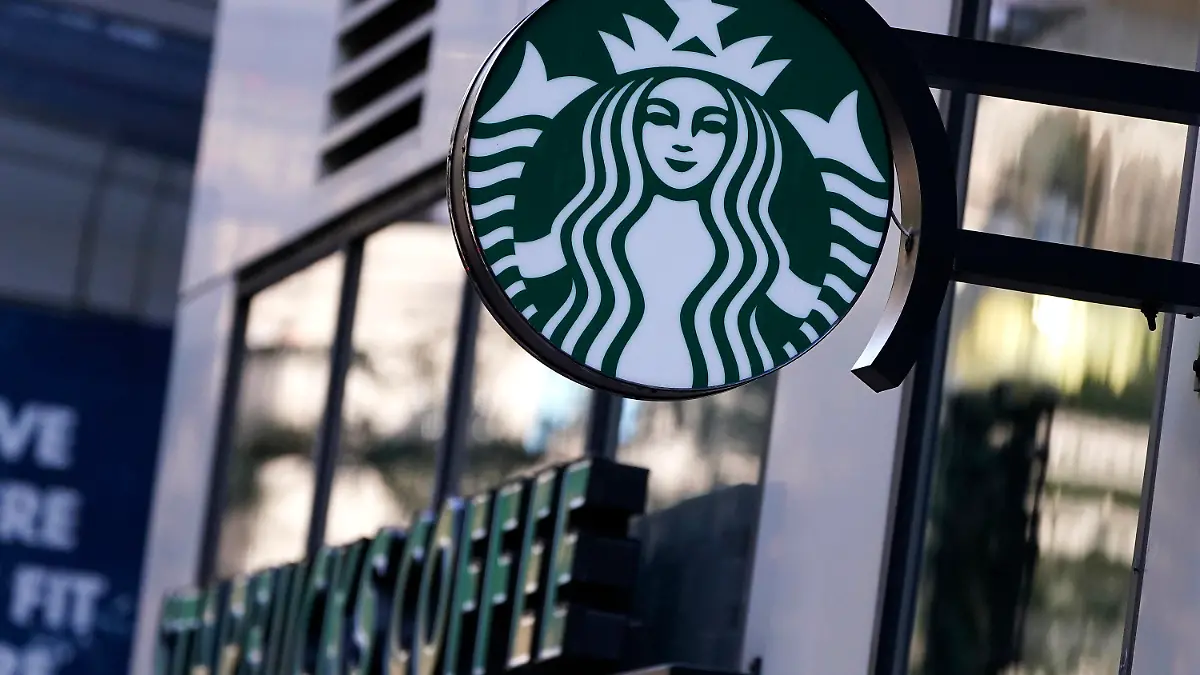 The "Siren" logo hangs outside a Starbucks Coffee shop, Wednesday, July 14, 2021, in Boston. Starbucks said Wednesday, Oct. 27 it is raising its U.S. employees’ pay and making other changes to improve working conditions in its stores.  (AP Photo/Charles Krupa)