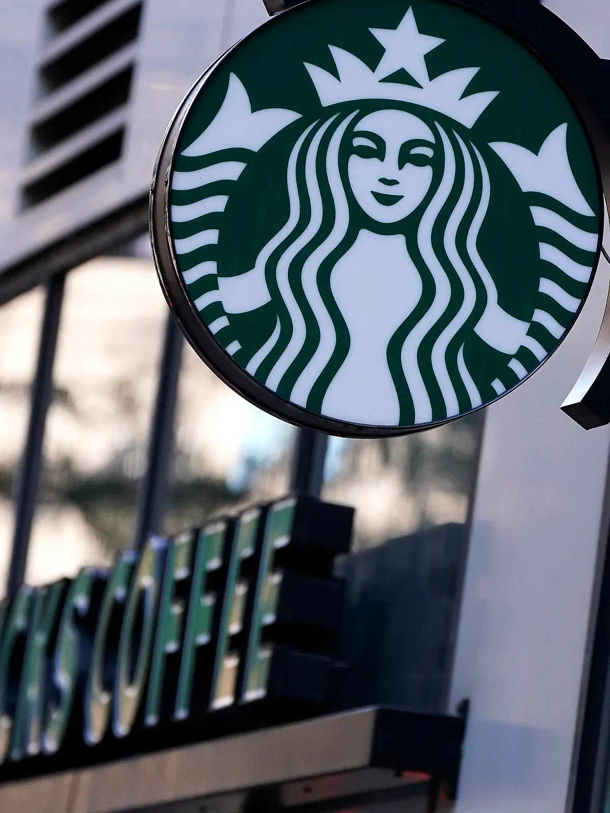 The "Siren" logo hangs outside a Starbucks Coffee shop, Wednesday, July 14, 2021, in Boston. Starbucks said Wednesday, Oct. 27 it is raising its U.S. employees’ pay and making other changes to improve working conditions in its stores.  (AP Photo/Charles Krupa)