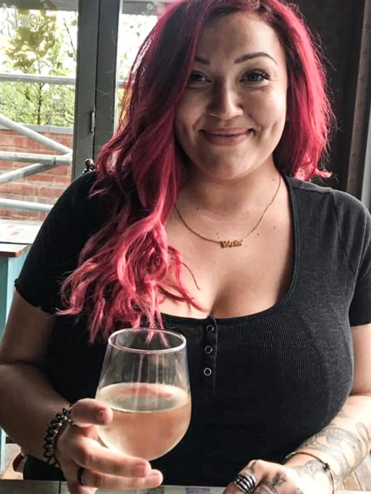 Engländerin Shade sitzt an einem Tisch vor ihr ein Glas Wein.