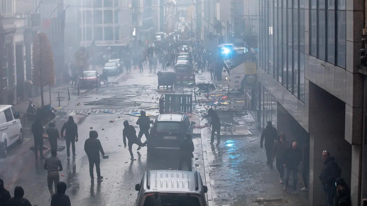 21.11.2021, Belgien, Brüssel: Demonstranten gehen auf einer Straße, auf der Trümmer und Steine liegen. Nach Polizeiangaben sind in Brüssel rund 35.000 Personen auf die Straße gegangen, um gegen die Coronamaßnahmen der Regierung zu demonstrieren. Bei Zusammenstößen musste die Polizei Wasserwerfer und Tränengas einsetzen. Foto: Hatim Kaghat/BELGA/dpa +++ dpa-Bildfunk +++