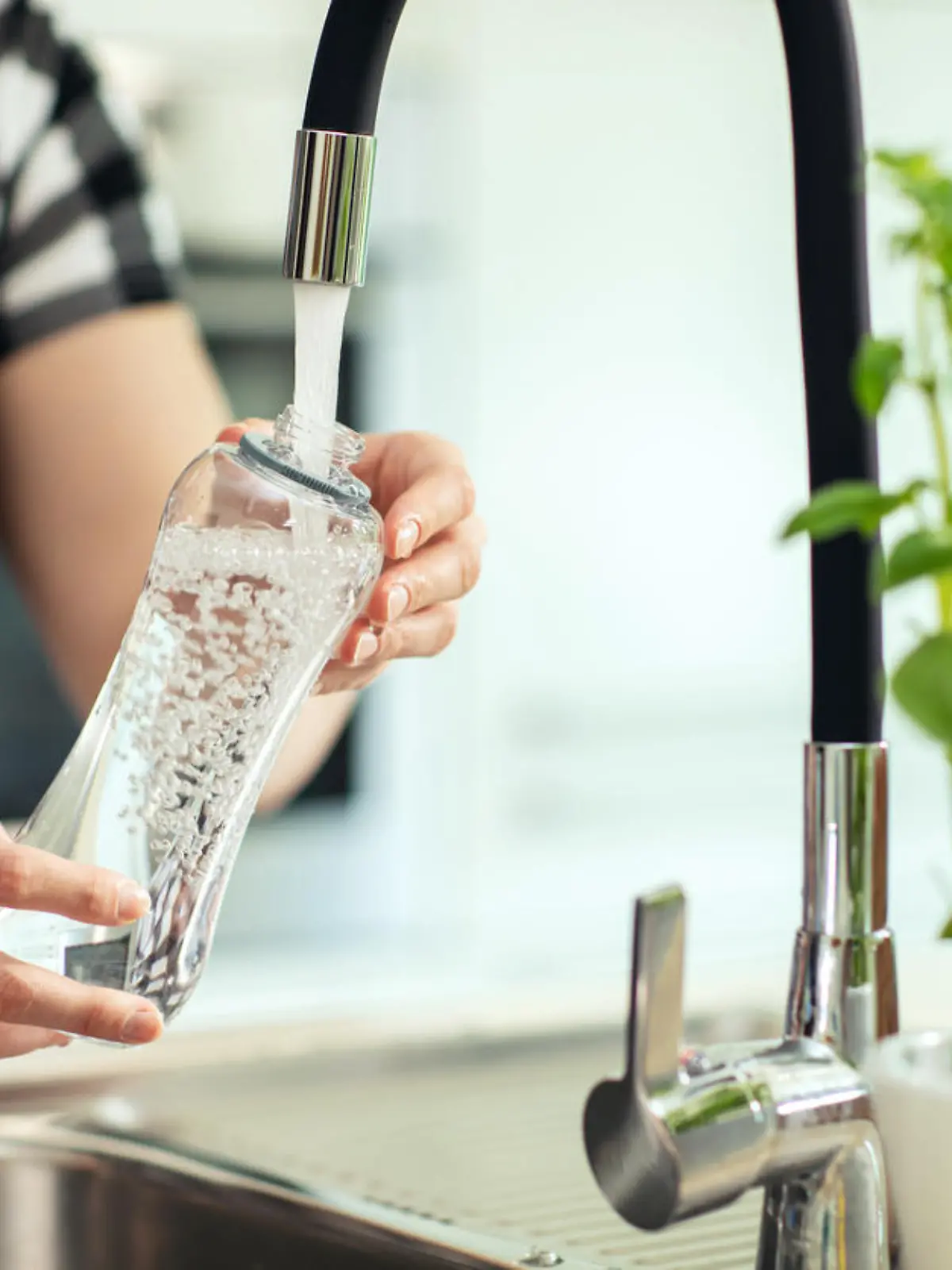 Pouring water into the bottle. Woman in background pours water from the sink to the reusable bottle