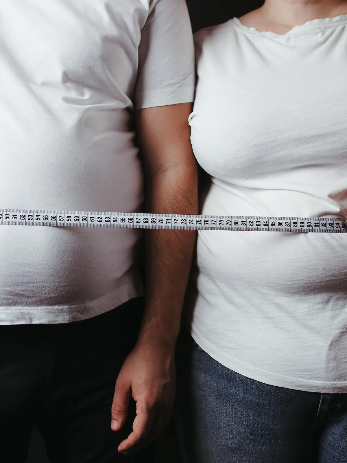 Overweight couple standing together wrapped with measure tape. Dieting, family weight loss and health care