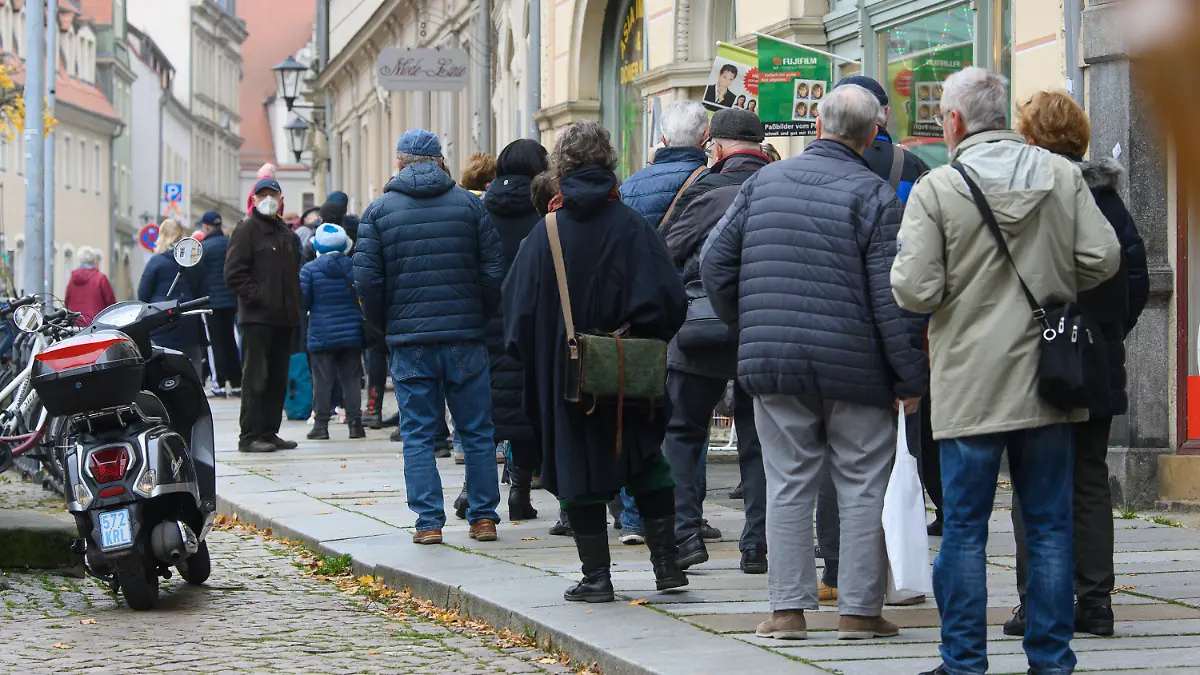 15.11.2021, Sachsen, Pirna: Zahlreiche Menschen stehen bei einer Impfaktion des DRK vor dem Stadthaus auf dem Markt der Stadt im Landkreis Sächsische Schweiz-Osterzgebirge in einer Warteschlange an um sich gegen das Coronavirus impfen zu lassen. Das Robert Koch-Institut (RKI) ermittelte am Montag eine Sieben-Tage-Inzidenz von 754,3. Im Landkreis Sächsische Schweiz-Osterzgebirge lag der Wert am Sonntagmorgen bei 1303,1. Er ist damit der Landkreis mit der höchsten bundesweiten Inzidenz. Foto: Robert Michael/dpa-Zentralbild/dpa +++ dpa-Bildfunk +++