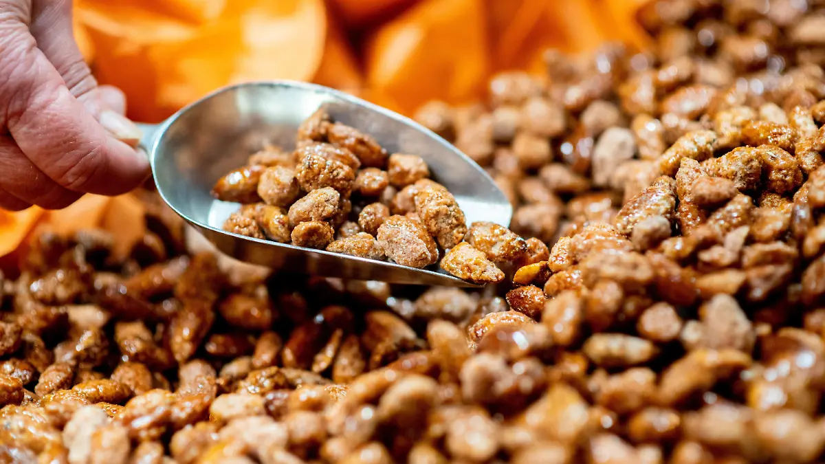 16.11.2021, Niedersachsen, Oldenburg: Eine Verkäuferin portioniert gebrannte Mandeln an einem Stand auf dem Lamberti-Markt. Der Weihnachtsmarkt in der Innenstadt wird am 16.11.2021 eröffnet, es gilt eine 3G-Pflicht. Auf dem Oldenburger Lamberti-Markt kommen deshalb Bändchen zum Einsatz, die die Gäste berechtigen, Speisen und Getränke zu kaufen. Foto: Hauke-Christian Dittrich/dpa +++ dpa-Bildfunk +++
