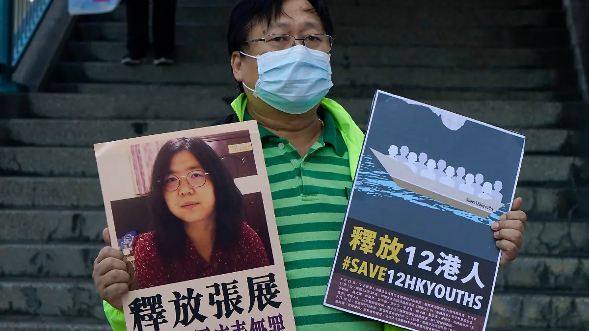 28.12.2020, China, Hongkong: Ein pro-demokratischer Aktivist zeigt zwei Plakate vor dem Verbindungsbüro der chinesischen Zentralregierung. Auf einem Plakat ist ein Foto der chinesischen Journalistin Zhang Zhan zu sehen. Zhang, eine ehemalige Anwältin und Journalistin aus Shanghai, wurde wegen ihrer Berichterstattung über den ersten Ausbruch des Coronavirus in Wuhan zu vier Jahren Gefängnis verurteilt. Die Aktivisten fordern die Freilassung von Zhang, sowie der 12 Hongkonger Aktivisten, die von den chinesischen Behörden auf See festgehalten werden. Foto: Kin Cheung/AP/dpa +++ dpa-Bildfunk +++