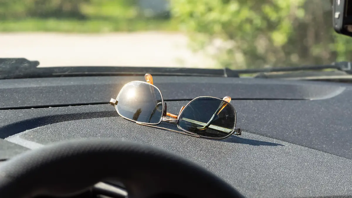 Sunglasses lie on the dashboard of a car while waiting for a ride.