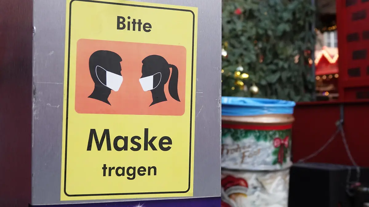 18.11.2021, Nordrhein-Westfalen, Düsseldorf: Auf einem Desinfektionsmittelspender hängt ein Schild mit der Aufschrift «Bitte Maske tragen». Trotz steigender Inzidenzen hat der Weihnachtsmarkt in der Landeshauptstadt am Donnerstag eröffnet. Auf dem Rathausplatz gibt es Einlasskontrollen, rein kommt nur, wer gegen Corona geimpft oder genesen ist. Foto: Mona Wenisch/dpa +++ dpa-Bildfunk +++
