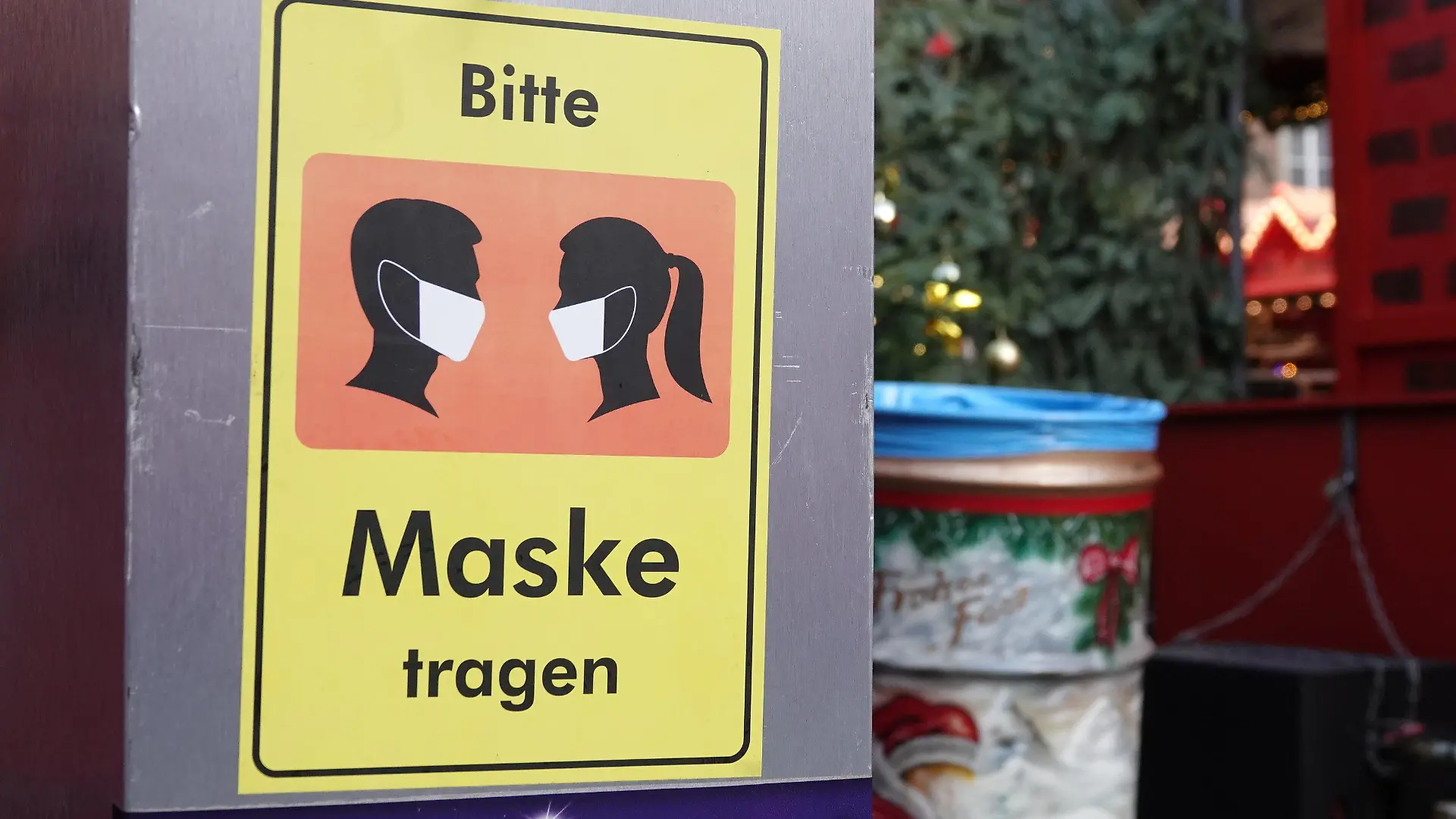 18.11.2021, Nordrhein-Westfalen, Düsseldorf: Auf einem Desinfektionsmittelspender hängt ein Schild mit der Aufschrift «Bitte Maske tragen». Trotz steigender Inzidenzen hat der Weihnachtsmarkt in der Landeshauptstadt am Donnerstag eröffnet. Auf dem Rathausplatz gibt es Einlasskontrollen, rein kommt nur, wer gegen Corona geimpft oder genesen ist. Foto: Mona Wenisch/dpa +++ dpa-Bildfunk +++