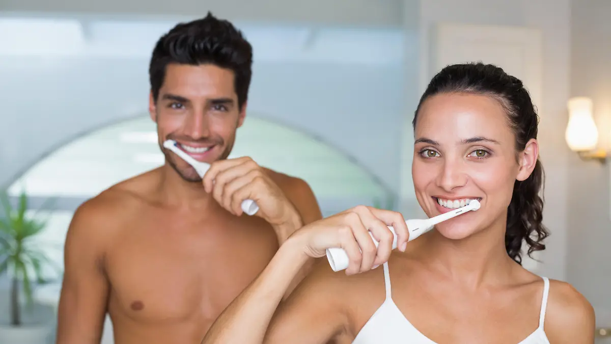 Attractive couple smile while using electric toothbrushes at home in bathroom
