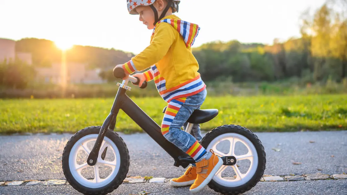 Caucasian boy with sports helmets driving balance bike outdoors on a sunny day. He is learning new skill.