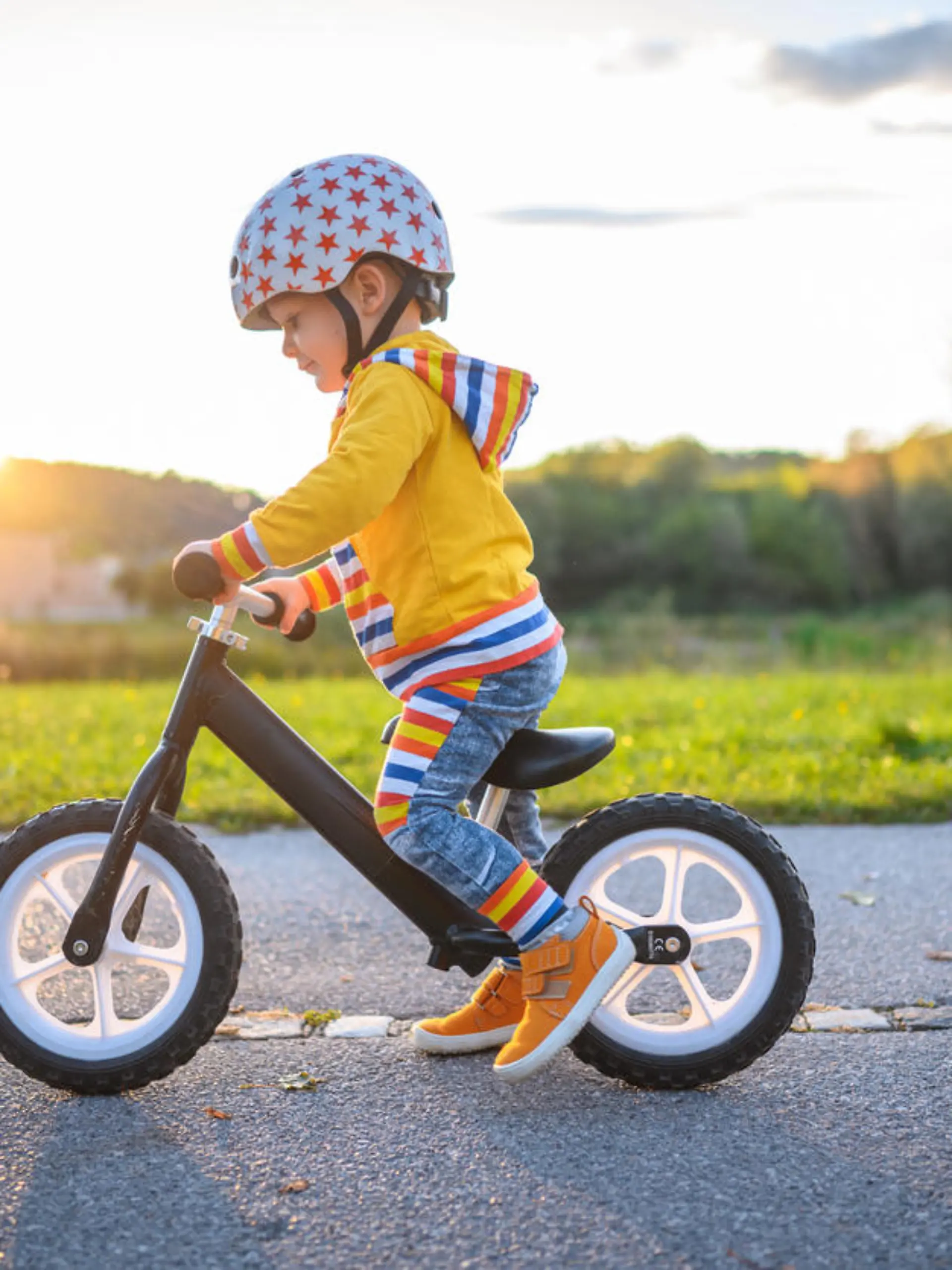 Caucasian boy with sports helmets driving balance bike outdoors on a sunny day. He is learning new skill.
