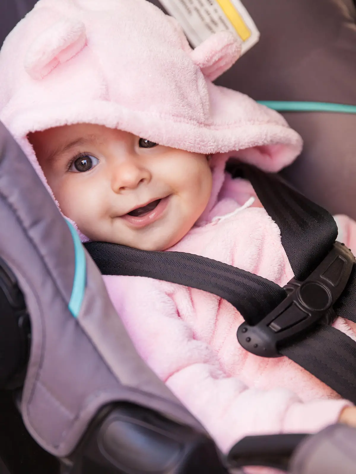 Kleines Mädchen sitzt glücklich im Autokindersitz.