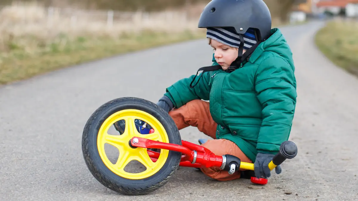 Adorable little toddler boy sad about his broken bicycle, sitting outdoors on the street