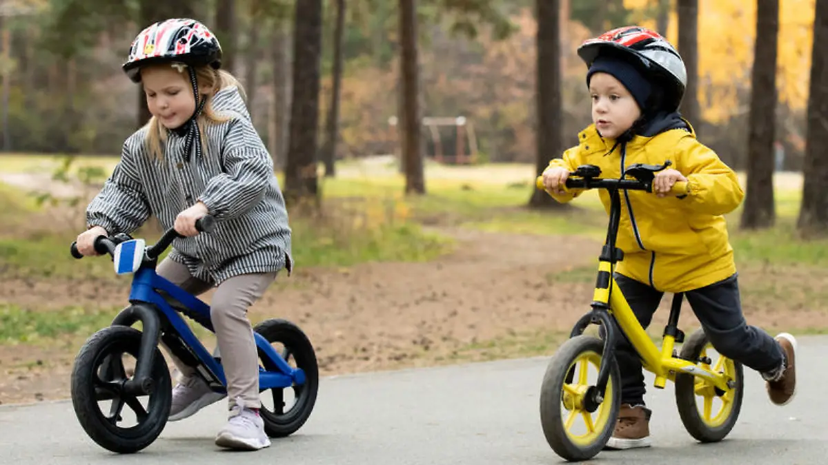 Two cute little boys and adorable blond girl sitting on their balance bikes while moving down asphalt road in natural environment at leisure