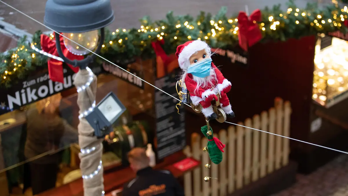 15.11.2021, Niedersachsen, Osnabrück: Ein kleiner radelnder Weihnachtsmann mit Maske bewegt sich auf einem Seil über den Köpfen der Besucher. Für den Weihnachtsmarkt gilt eine 2G-Pflicht. Auf dem Osnabrücker Weihnachtsmarkt kommen deshalb Bändchen zum Einsatz, die die Gäste berechtigen, Speisen und Getränke zu kaufen. Dazu muß vorher nachgewiesen werden, ob man vollständig geimpft oder genesen ist. Foto: Friso Gentsch/dpa +++ dpa-Bildfunk +++
