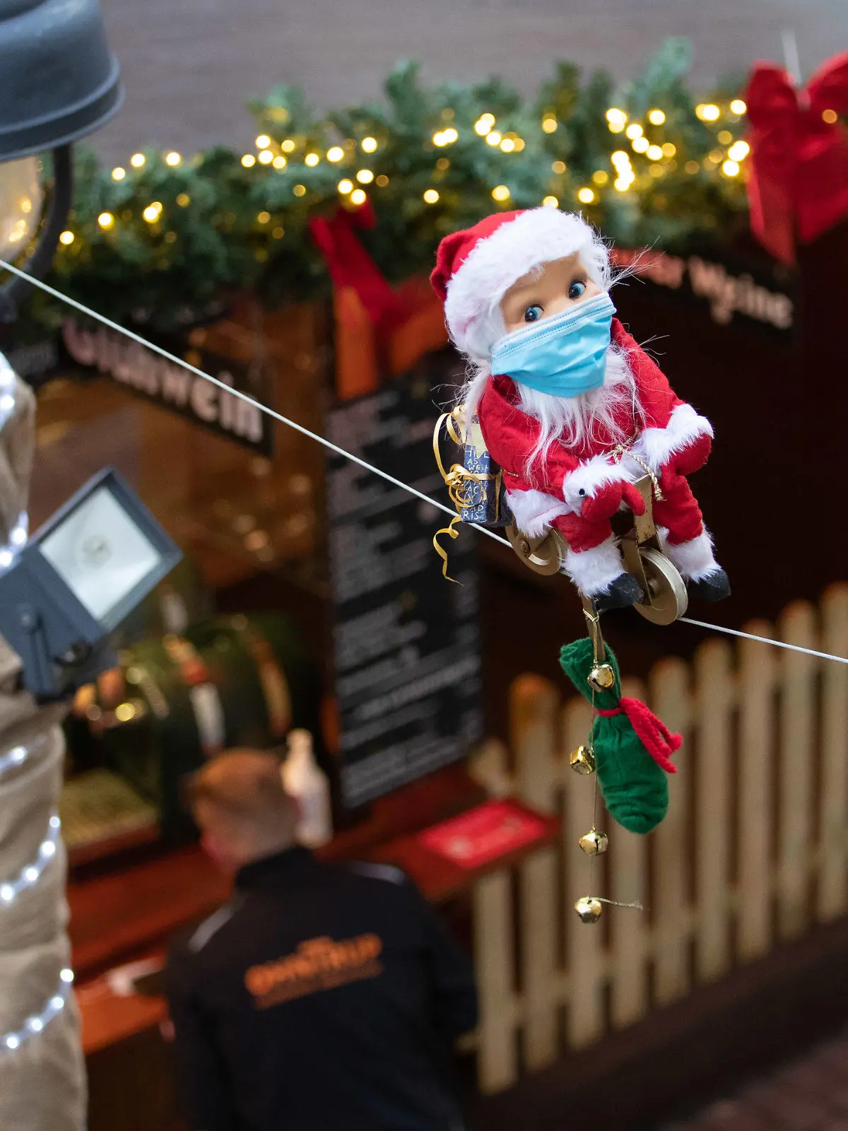 15.11.2021, Niedersachsen, Osnabrück: Ein kleiner radelnder Weihnachtsmann mit Maske bewegt sich auf einem Seil über den Köpfen der Besucher. Für den Weihnachtsmarkt gilt eine 2G-Pflicht. Auf dem Osnabrücker Weihnachtsmarkt kommen deshalb Bändchen zum Einsatz, die die Gäste berechtigen, Speisen und Getränke zu kaufen. Dazu muß vorher nachgewiesen werden, ob man vollständig geimpft oder genesen ist. Foto: Friso Gentsch/dpa +++ dpa-Bildfunk +++