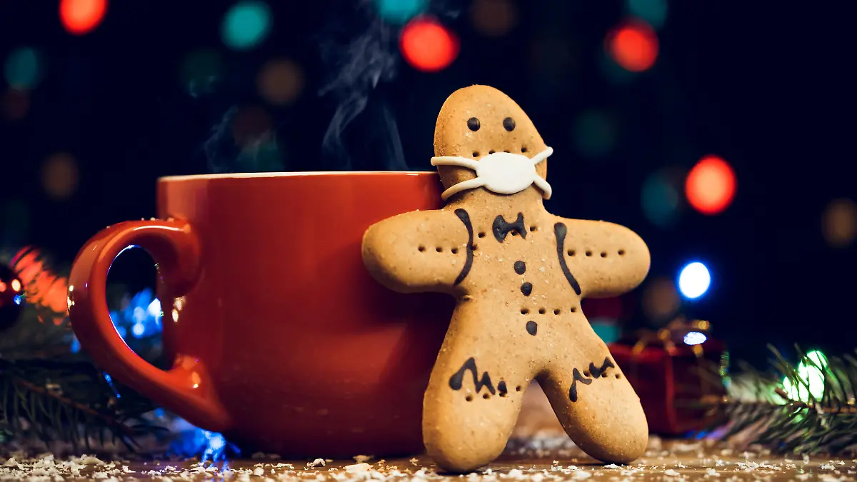 Gingerbread cookie wearing face mask and red cup on Christmas background