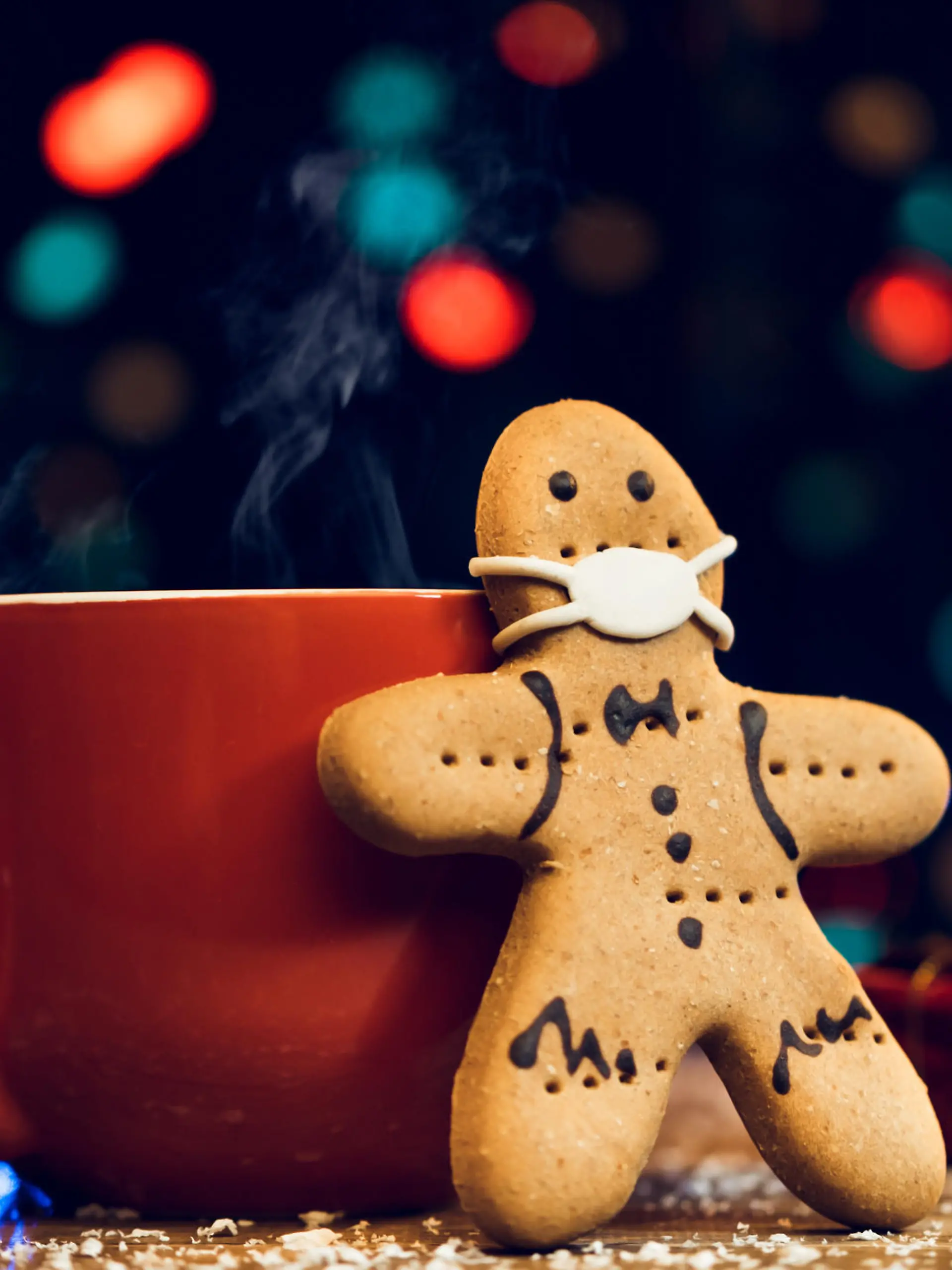 Gingerbread cookie wearing face mask and red cup on Christmas background