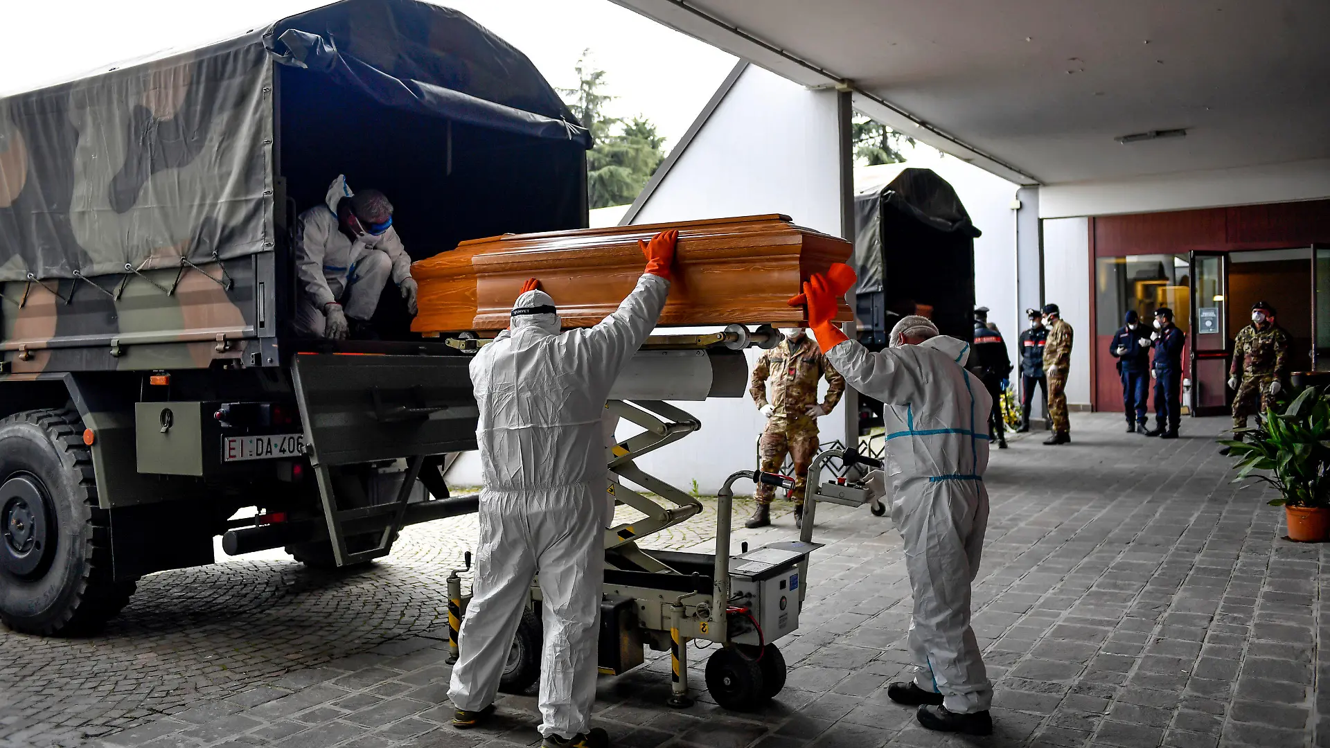 27.03.2020, Italien, Cinisello Balsamo: Särge, die aus der Gegend von Bergamo eintreffen, werden von Arbeitern in Schutzanzügen aus einem Militärfahrzeug in ein Gebäude des Friedhofs von Cinisello Balsamo getragen. Foto: Claudio Furlan/LaPresse/AP/dpa +++ dpa-Bildfunk +++