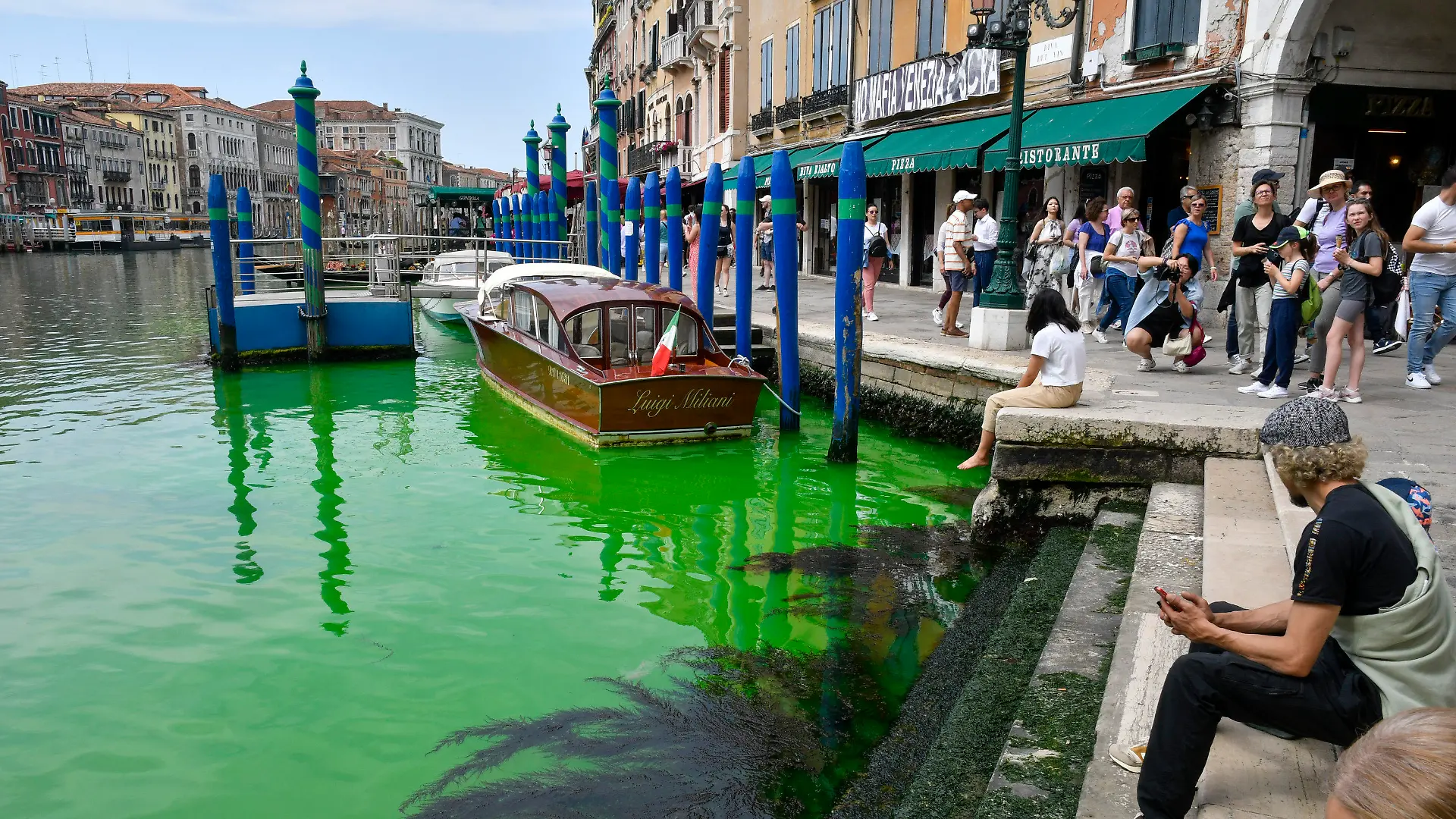 28.05.2023, Italien, Venedig: Menschen blicken auf den historischen Canal Grande in Venedig. Eine grün schimmernde Flüssigkeit im berühmten Canal Grande von Venedig hat für Aufregung in der Lagunenstadt gesorgt. Am Sonntag war das Wasser in der Nähe der Rialto-Brücke plötzlich grün. Die italienische Feuerwehr teilte mit, zusammen mit der Umweltschutzagentur Arpa Proben entnommen zu haben und diese zu untersuchen. Foto: Luigi Costantini/AP/dpa +++ dpa-Bildfunk +++