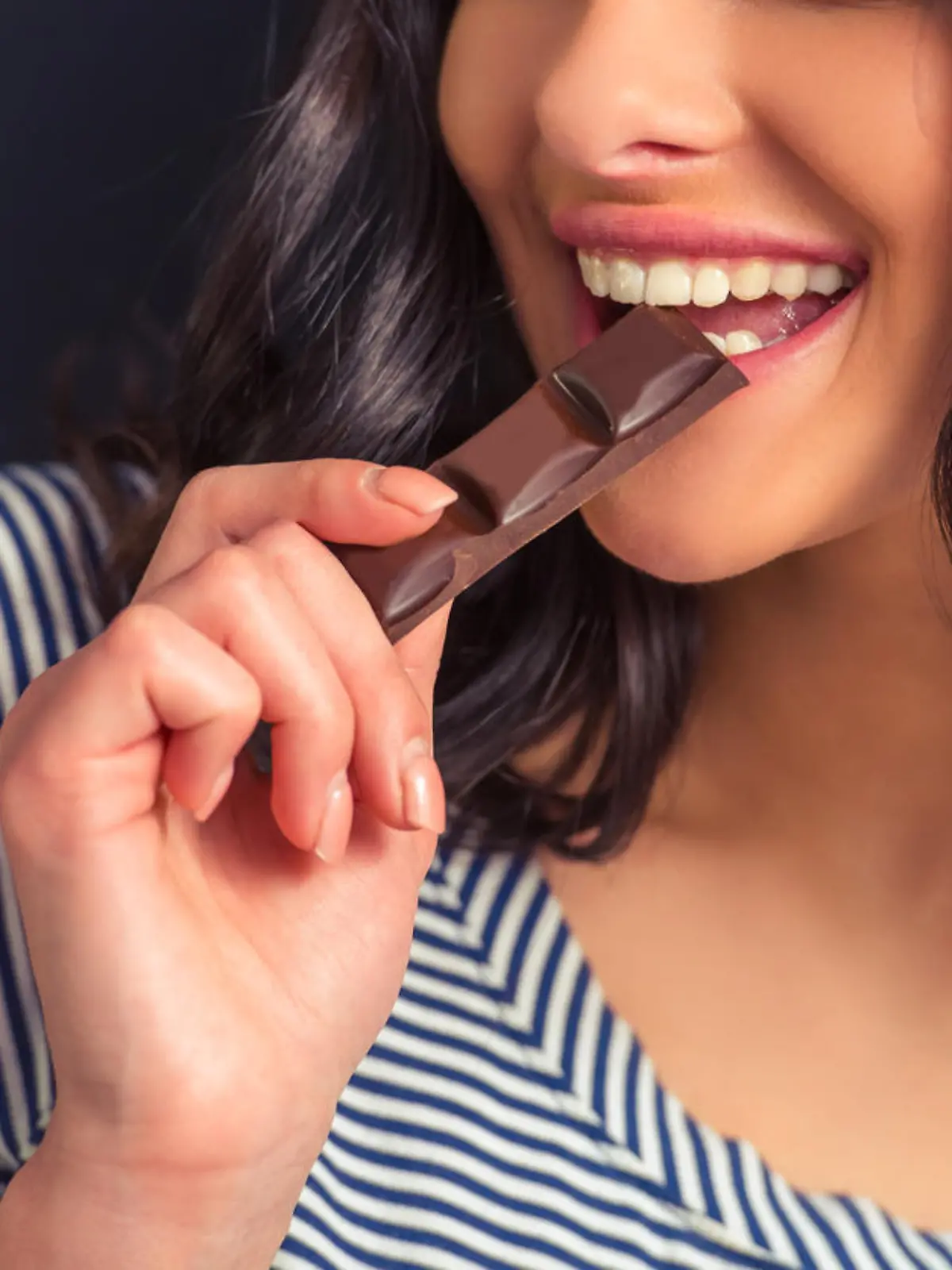 Cropped image of attractive girl eating chocolate and smiling, against dark background