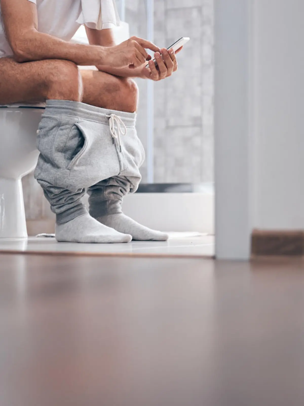 Cropped photo of a Caucasian male with a cellular phone sitting on the toilet seat