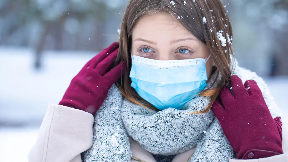 Young woman blue eyed girl posing on the snow with protective mask