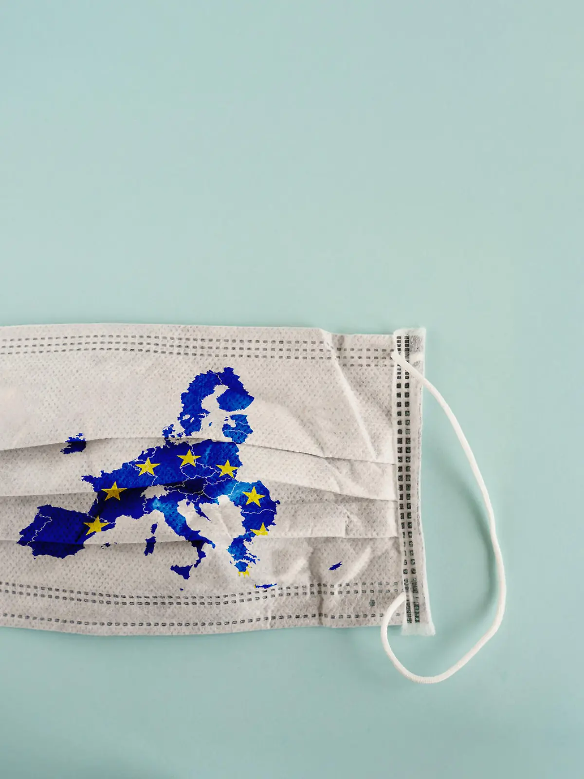 White medical mask with coronavirus word and European Union map on it isolated on cyan background. Face mask protection against pollution, virus, flu and coronavirus. Health care and surgical concept.