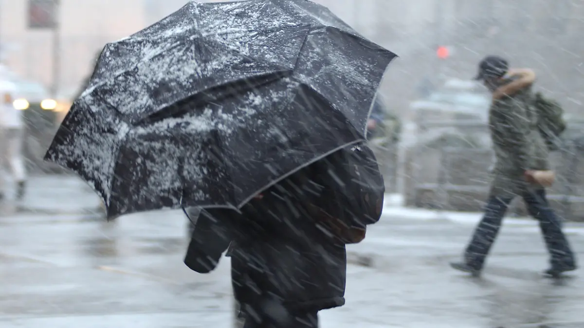 This is a photograph of a pedestrian in a snow storm with an aumbrella with a person in the background without an umbrella.