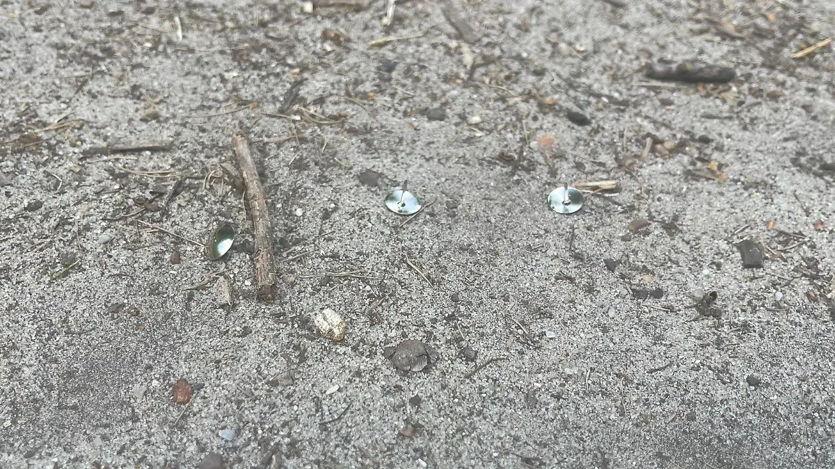 Reißzwecken liegen auf Sand.