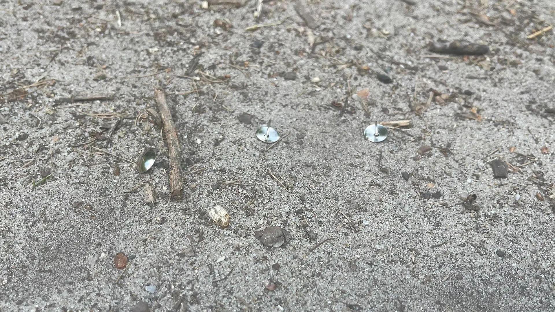 Reißzwecken liegen auf Sand.