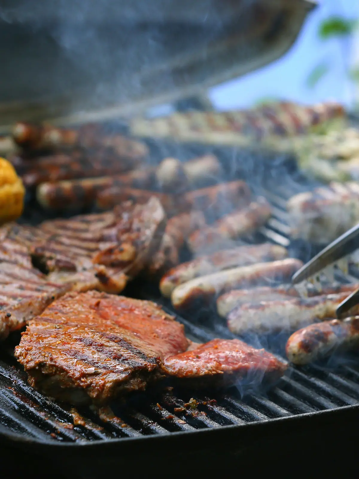 ARCHIV - 26.05.2018, Bayern, München: Maiskolben, Fleischspieße, Bratwürste und Steaks liegen auf dem Rost eines Gasgrills.   (zu dpa «Schweinenackensteak beliebtes Grillfleisch - Spezialitäten im Kommen» vom 04.08.2018) Foto: Karl-Josef Hildenbrand/dpa +++ dpa-Bildfunk +++