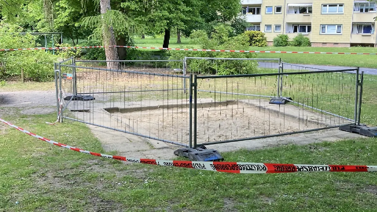 Ein Sandkasten ist von einem Bauzaun umstellt.