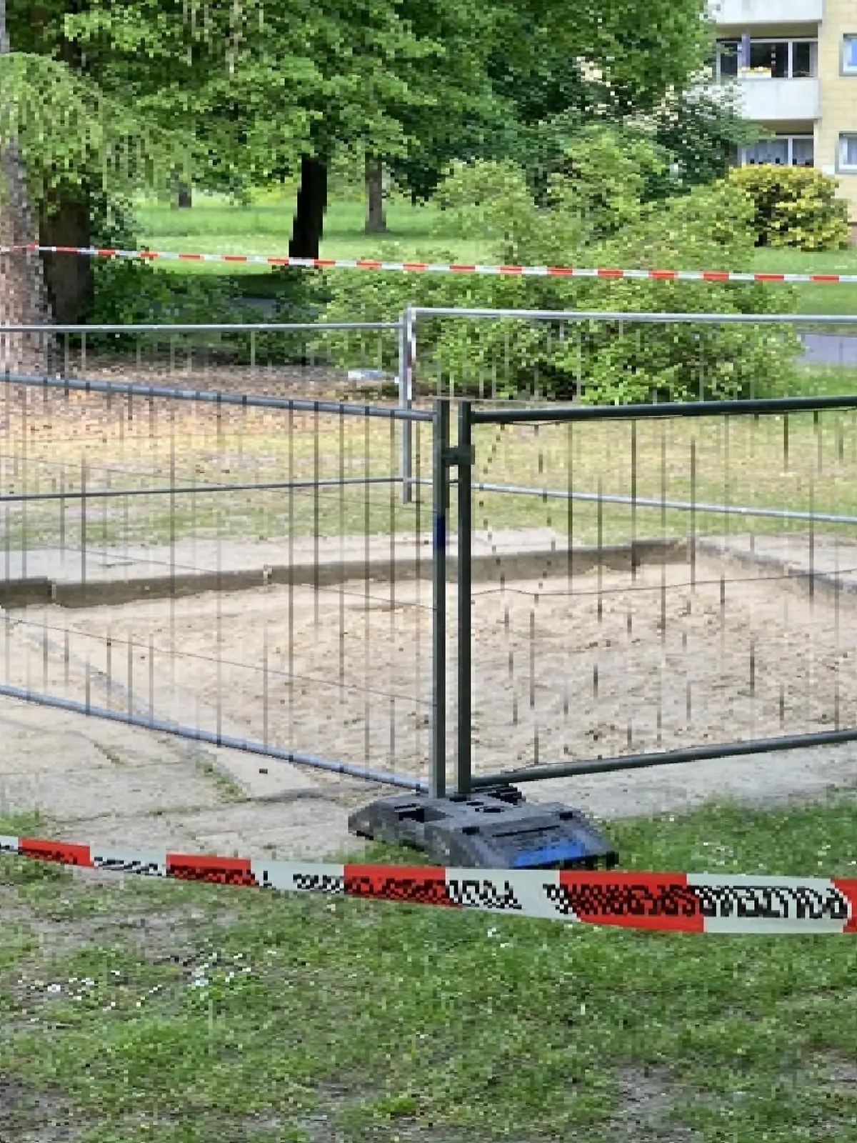 Ein Sandkasten ist von einem Bauzaun umstellt.