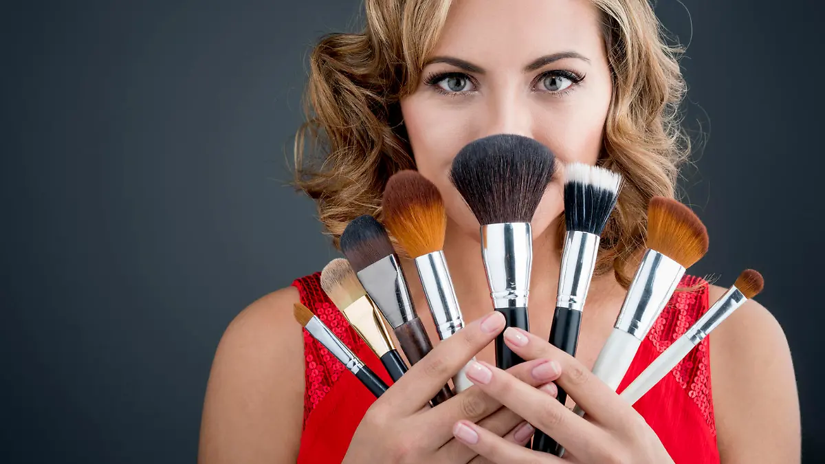 Excited woman holding makeup brushes and covering her face - beauty concepts