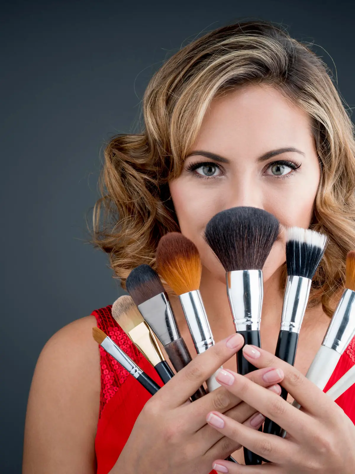 Excited woman holding makeup brushes and covering her face - beauty concepts