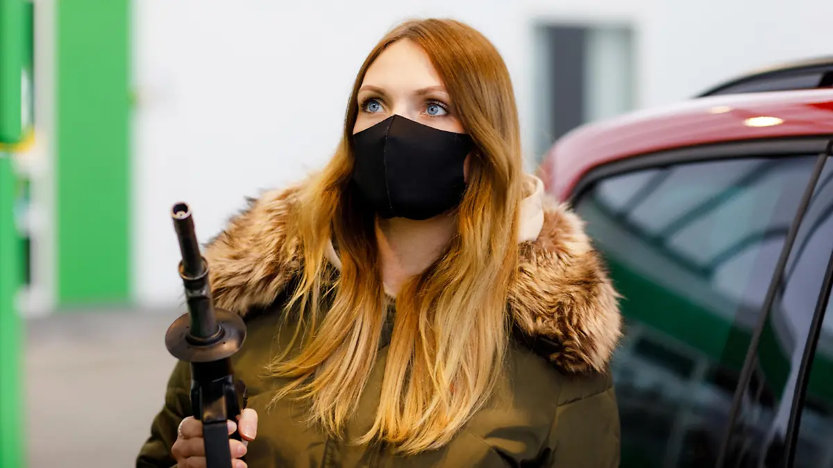 Woman wear medical mask at self-service gas station, hold fuel nozzle, refuel the car with petrol during corona virus pandemic lockdown. People in masks as preventive measure and covid protection.