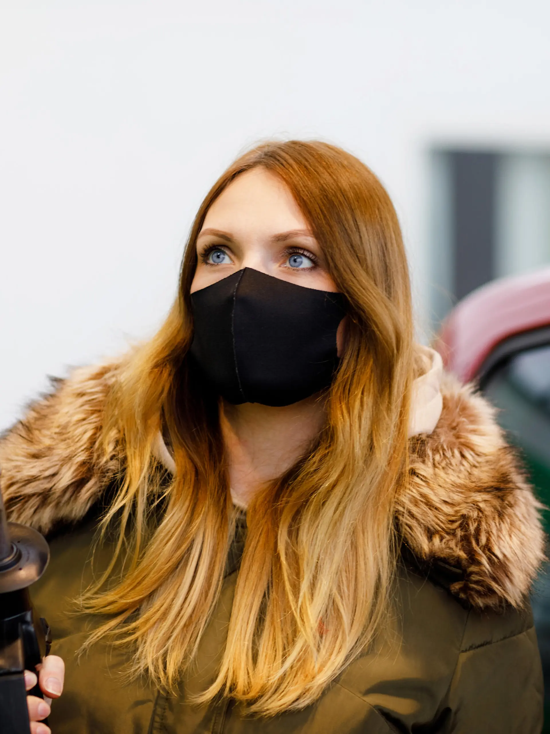 Woman wear medical mask at self-service gas station, hold fuel nozzle, refuel the car with petrol during corona virus pandemic lockdown. People in masks as preventive measure and covid protection.