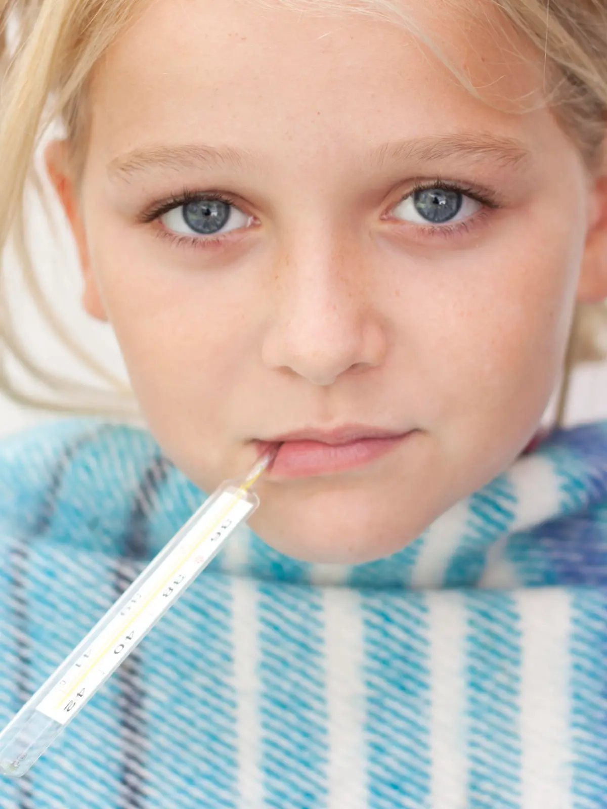 Close up of child with fever thermometer, wrapped in blanket