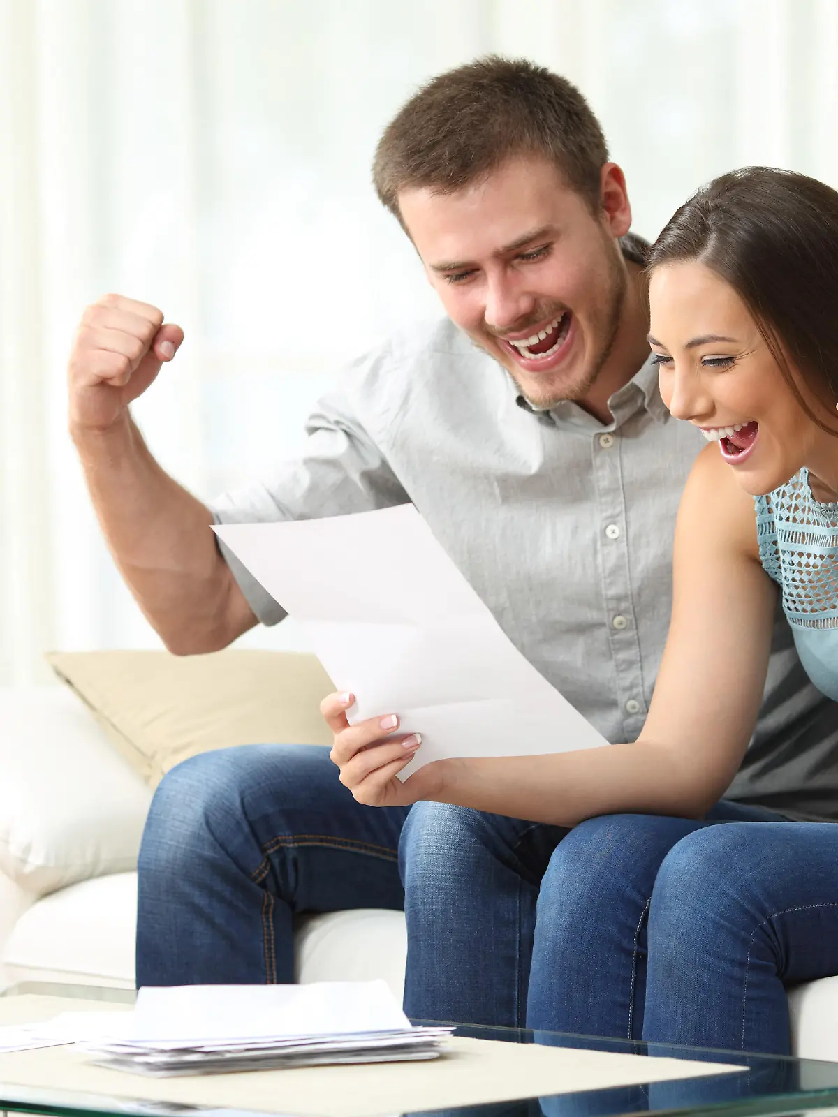 Excited couple reading a letter together sitting on a sofa in the living room at home