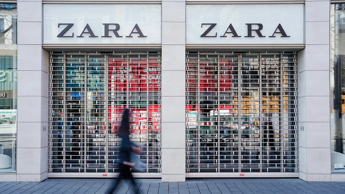 ARCHIV - 18.03.2020, Baden-Württemberg, Mannheim: Eine Fußgängerin geht vormittags in der Einkaufsstraße Planken an einem mit Gitter verschlossenen Eingang eines Zara-Bekleidungsgeschäfts vorbei. Der spanische Textilhändler Inditex ist wegen der Corona-Pandemie erstmals seit vielen Jahren in die roten Zahlen gerutscht. (zu dpa "Corona-Krise brockt Zara-Mutterkonzern Inditex Quartalsverlust ein") Foto: Uwe Anspach/dpa +++ dpa-Bildfunk +++